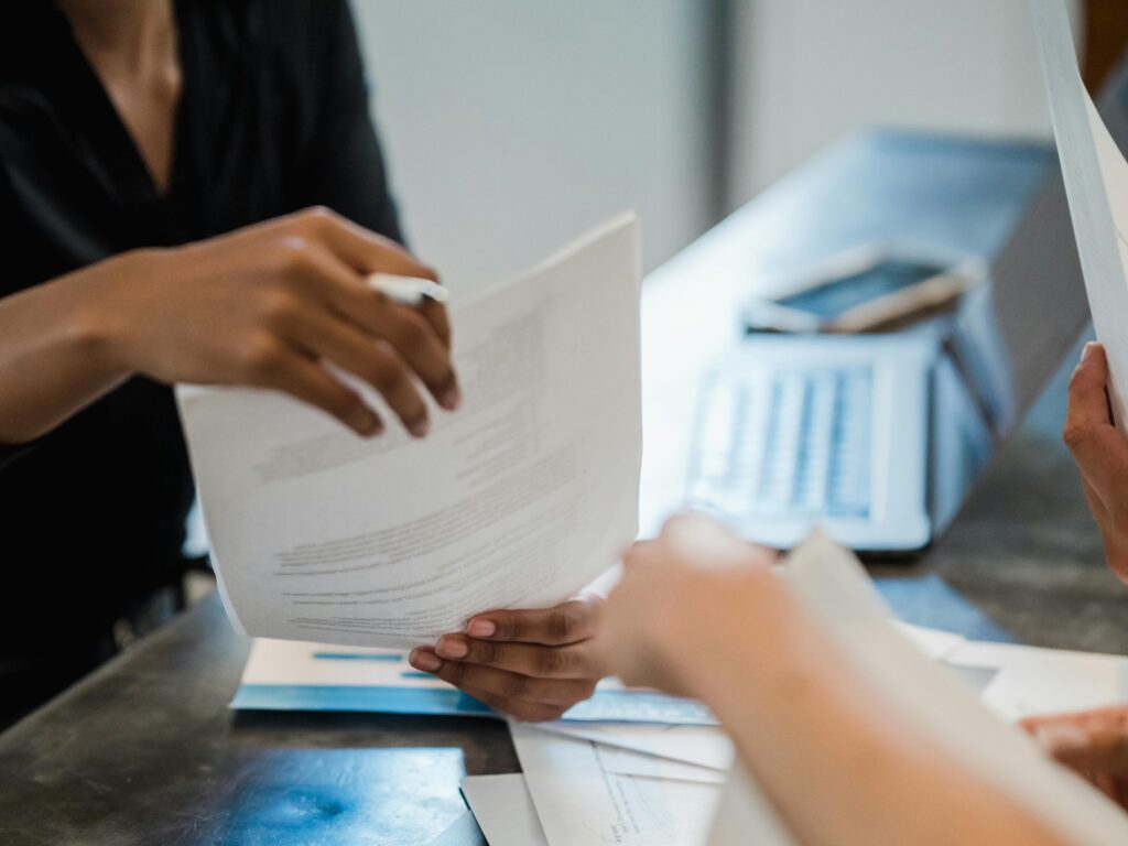 People reviewing documents at a desk with a laptop in the background.
