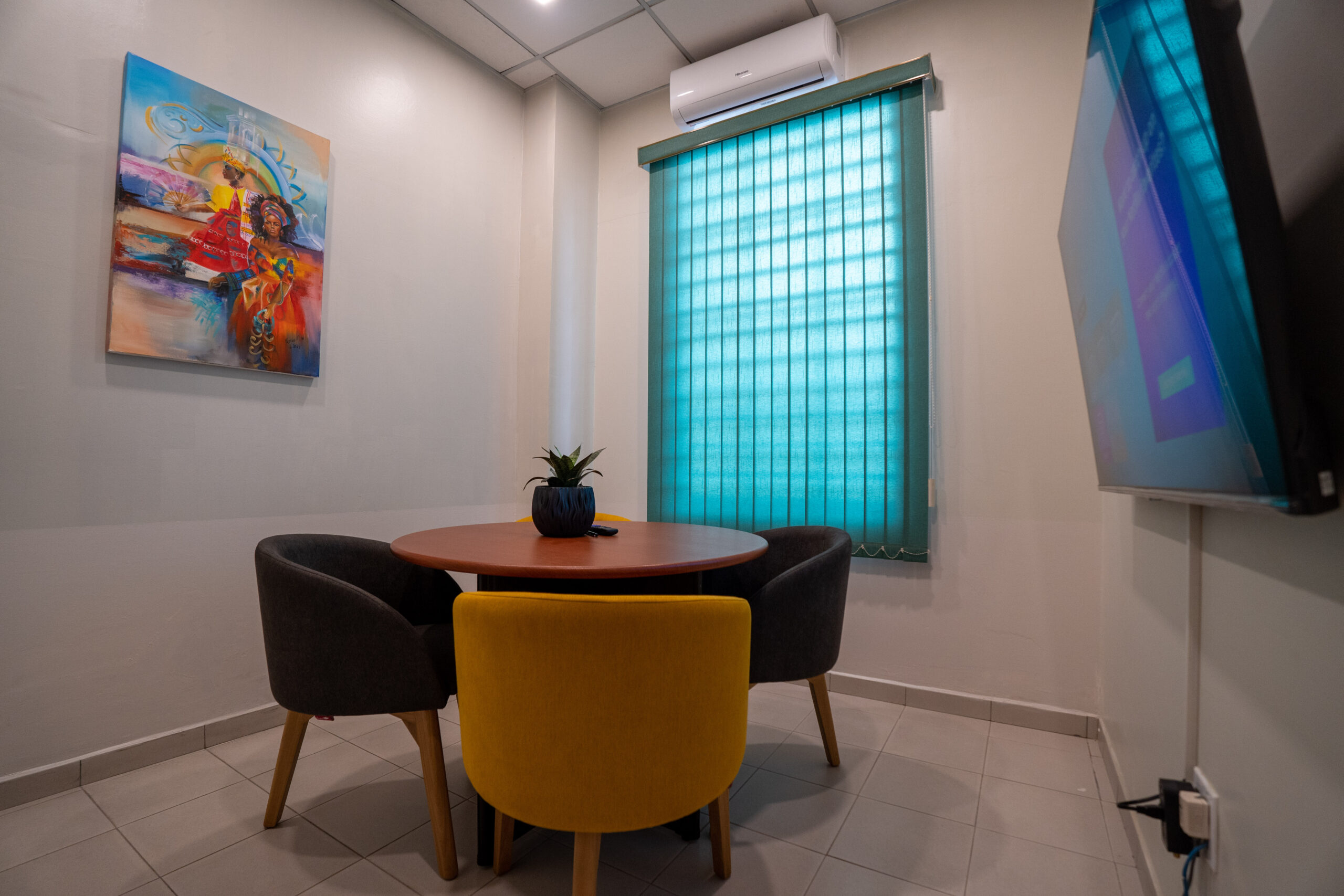Small meeting room with a round table, three chairs, and a wall-mounted TV.