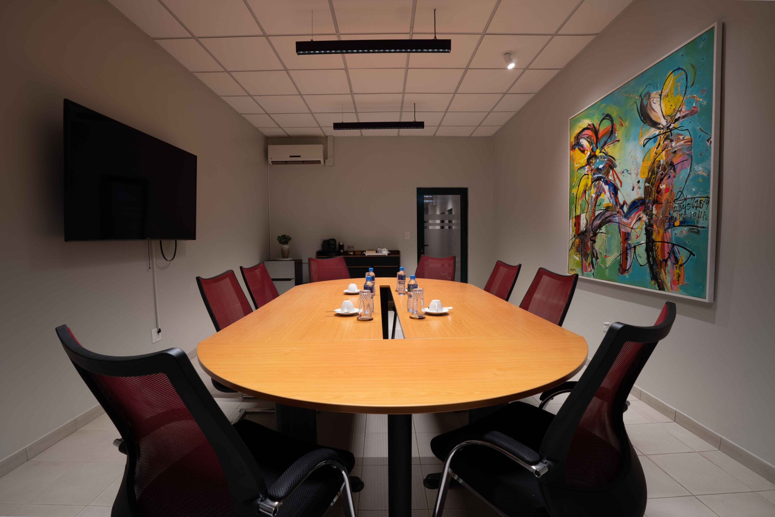 Conference room with a long table, chairs, and a large wall-mounted screen.